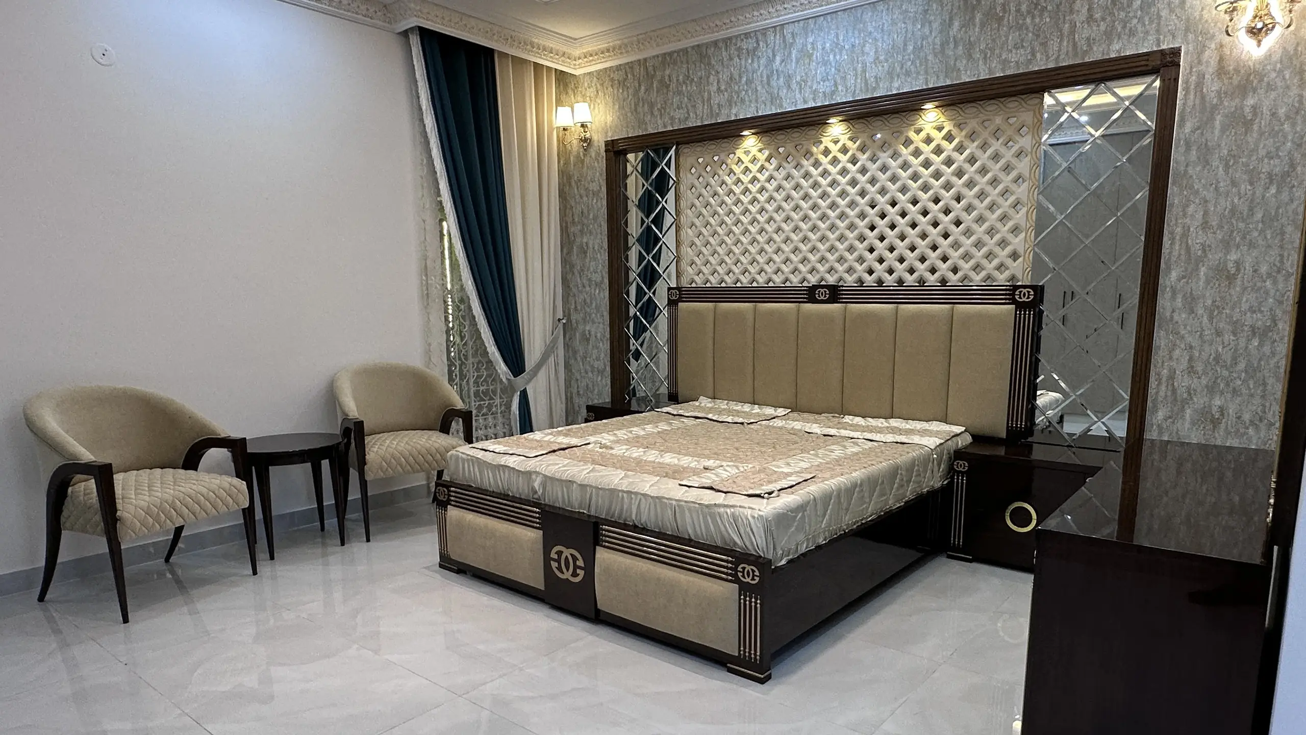 A wide view of a modern bedroom with an upholstered bed and a separate seating area with two chairs.