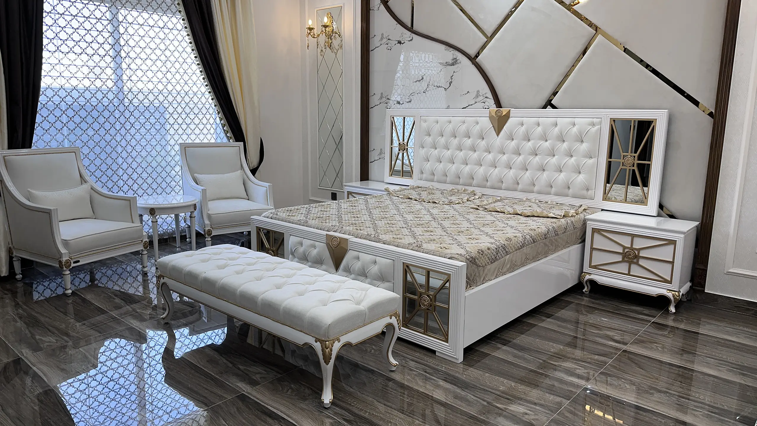 Full view of a luxury white and gold bedroom suite with a tufted bed and matching armchair.