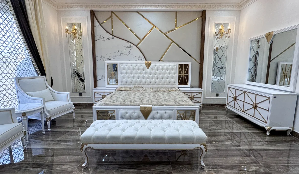 Luxurious white and gold bedroom set with a tufted bench and chairs against a geometric wall.