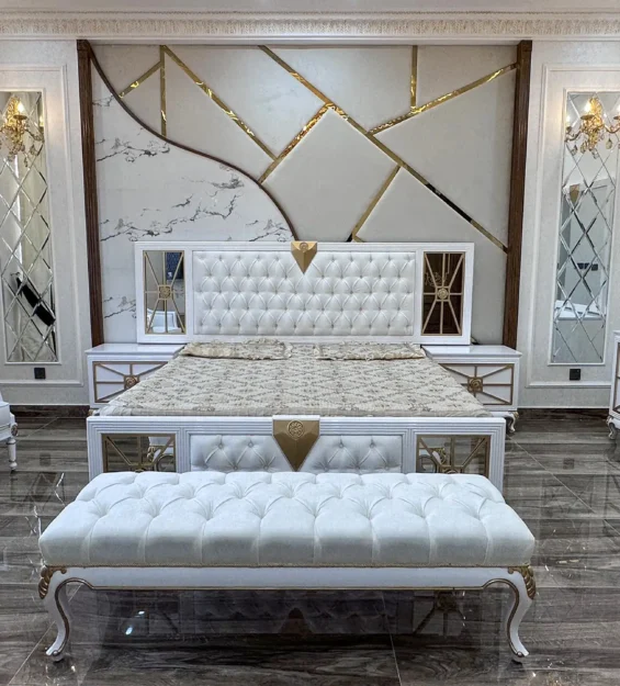 Luxurious white and gold bedroom set with a tufted bench and chairs against a geometric wall.