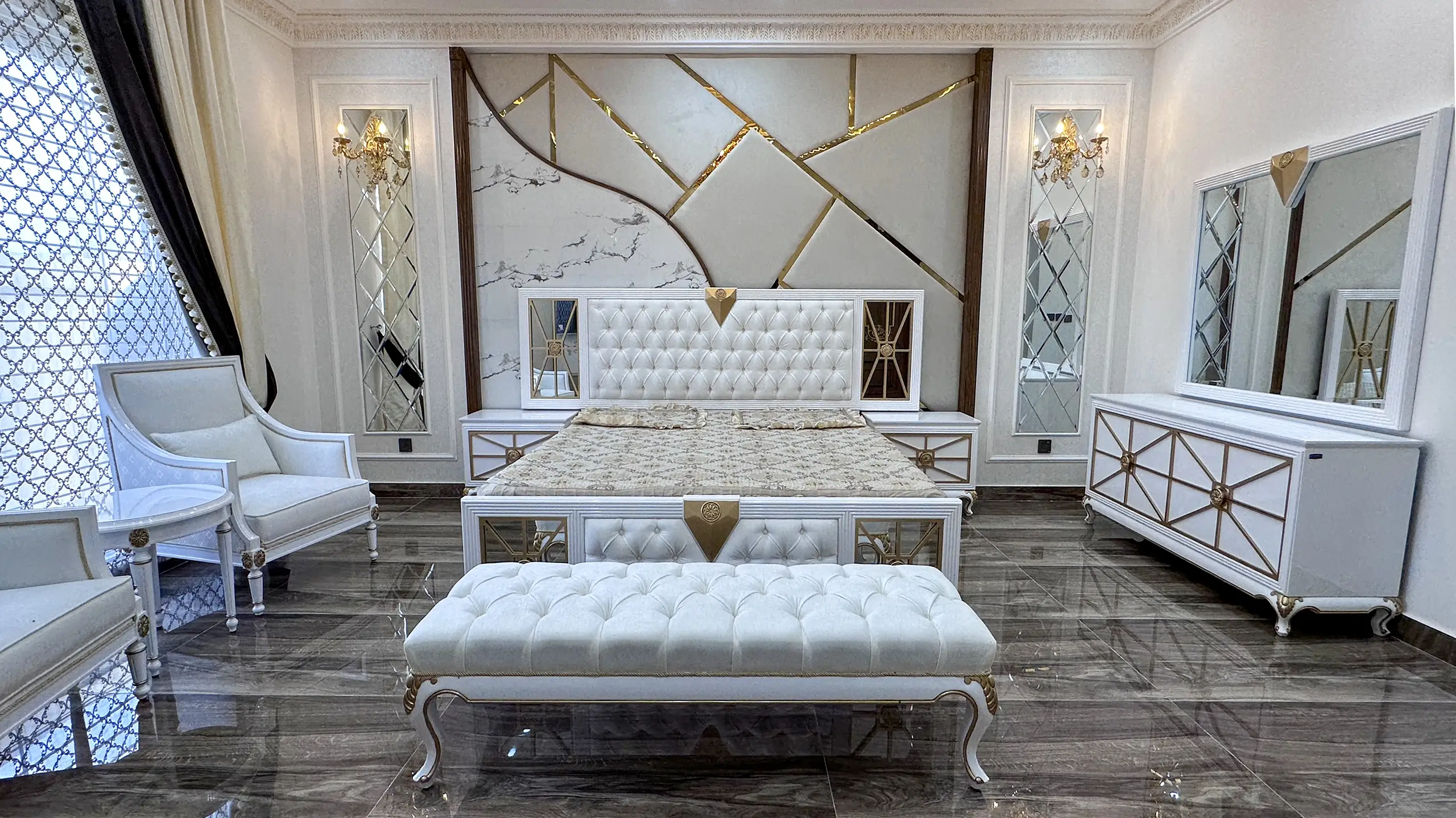 Luxurious white and gold bedroom set with a tufted bench and chairs against a geometric wall.