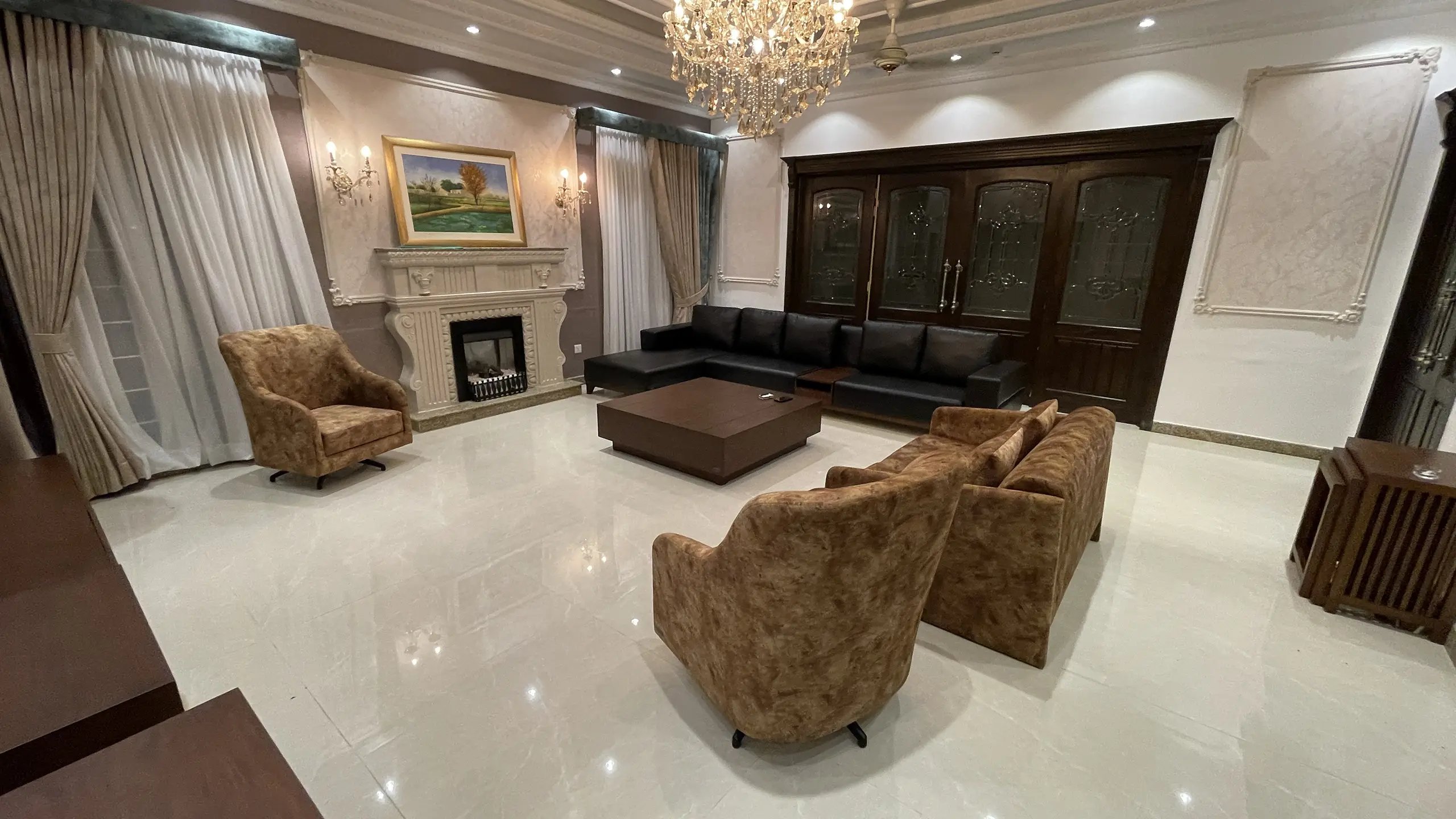 Grand living room featuring a black leather sofa, classic fireplace, and large crystal chandelier.
