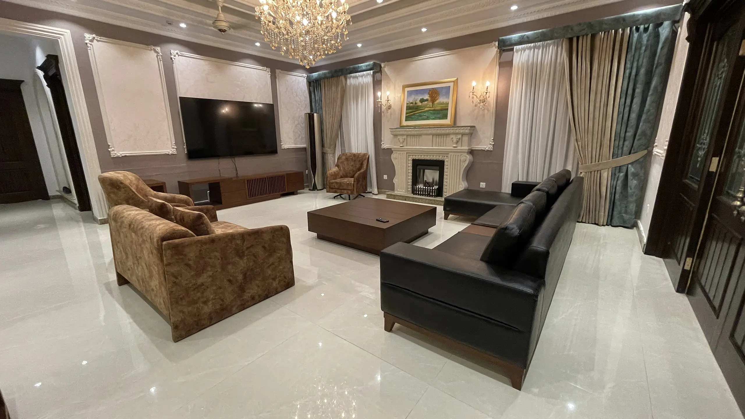 Wide view of an elegant living room with a fireplace, a black sofa, and brown armchairs.