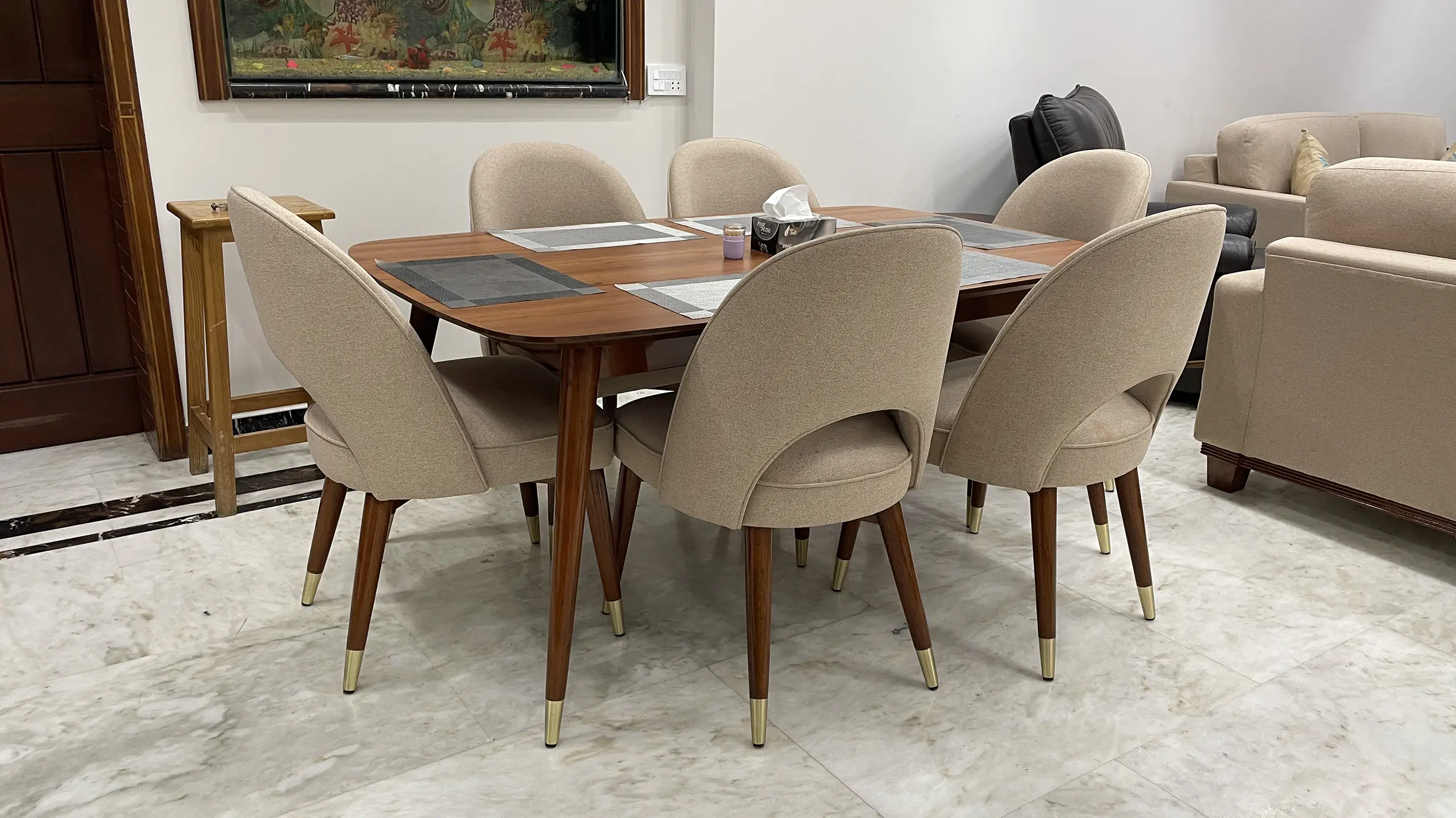 Modern six-seater dining table with beige upholstered chairs on a marble floor.