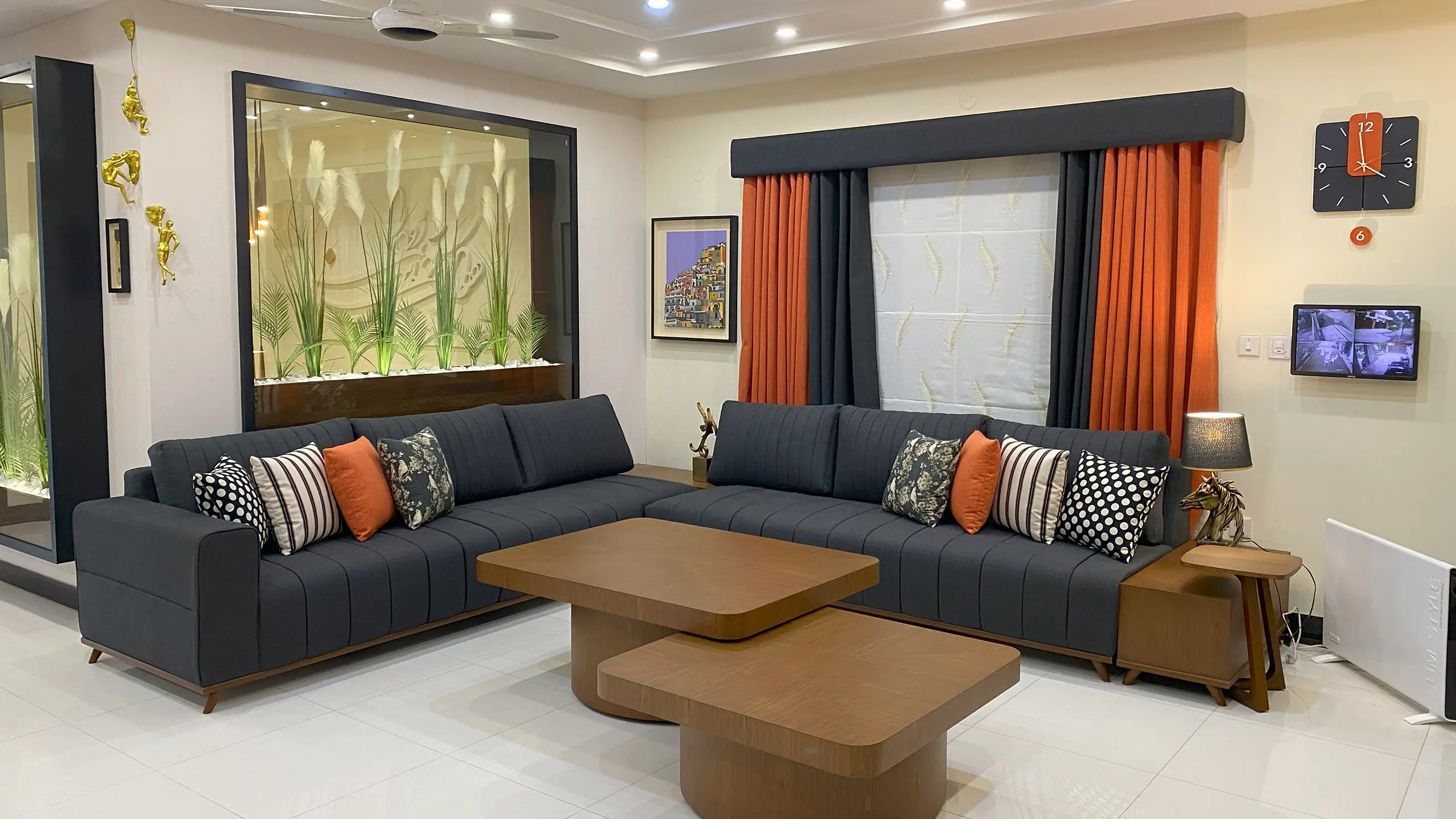 Contemporary living room featuring a large grey L-shaped sofa, modern coffee tables, and a large indoor planter.