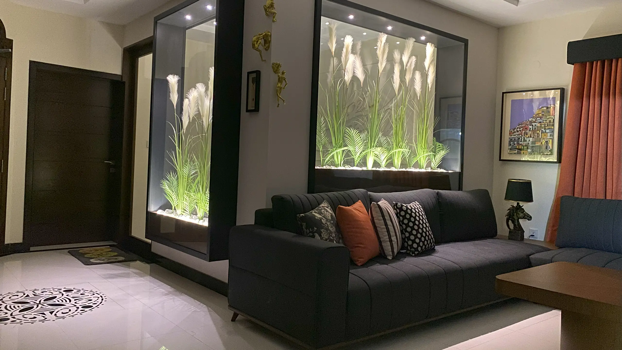 A modern living room with a dark grey sectional sofa and illuminated indoor glass planters.