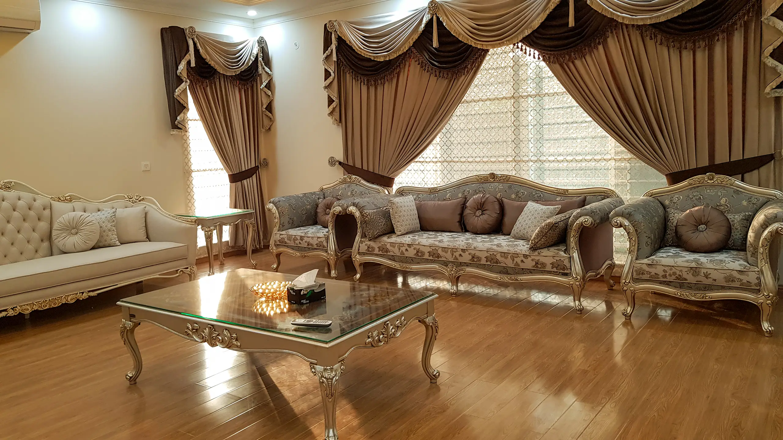 Luxurious formal living room with classic silver and grey floral upholstered sofas and matching tufted chairs.