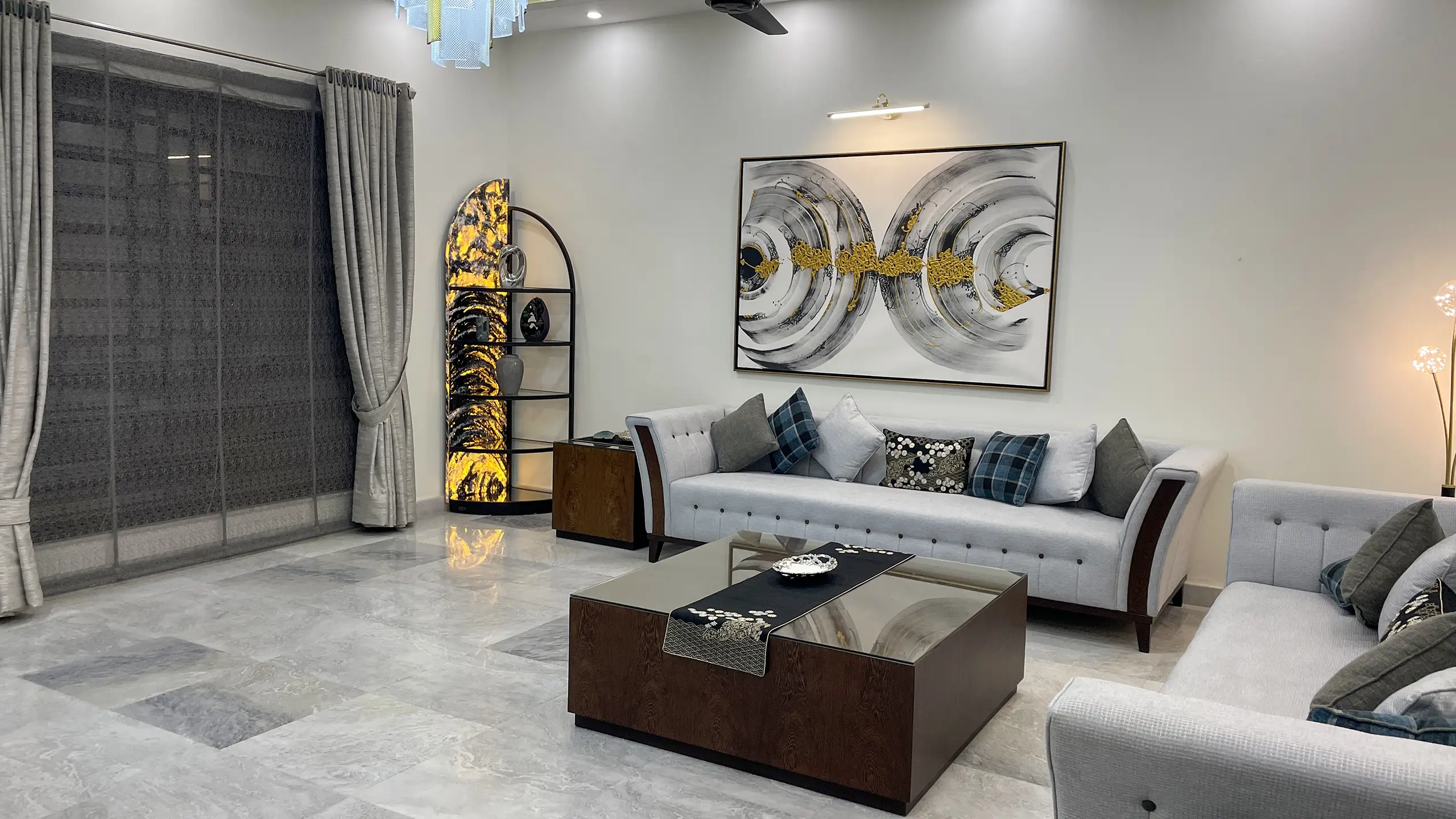 Side view of a modern living room with a light grey sofa, illuminated arched shelf, and abstract art.
