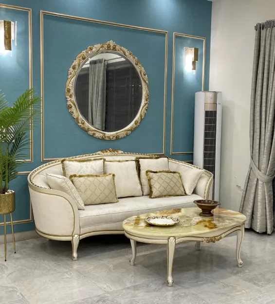 Classic living room with a curved off-white sofa, marble-top coffee table, and an ornate gold mirror on a teal wall.
