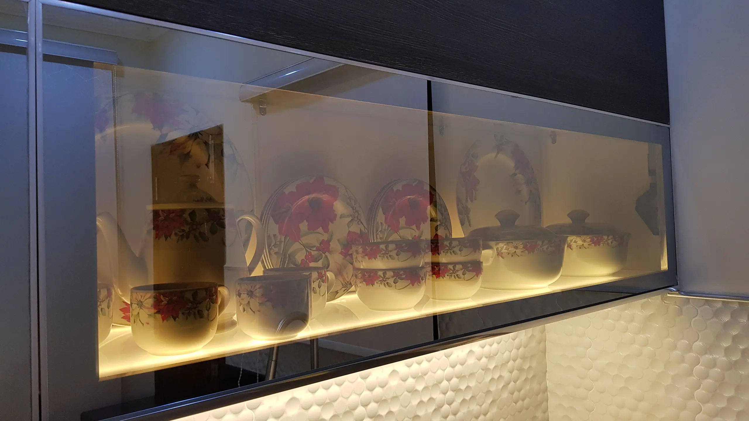 Glass kitchen cabinet with illuminated shelves displaying floral dinnerware.